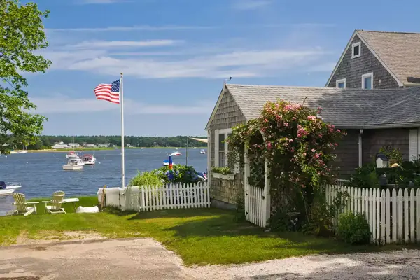 A seaside cottage on a quiet cove on Cape Cod features a, arbored gate covered with pink roses.
