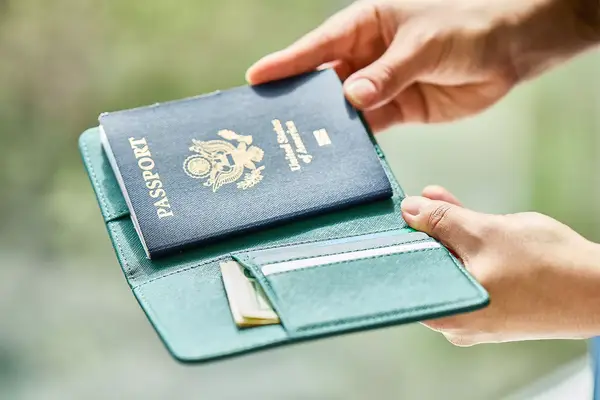 Hands holding an open wallet with a passport and additional documents