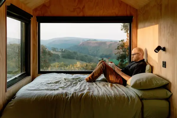 A man sits on a bed reading in a cabin