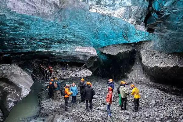 People stand beneath a blue-colored frozen glacier in a cave in Iceland 