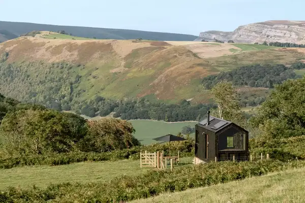 A black cabin sits in the countryside of Wales overlooking a hill