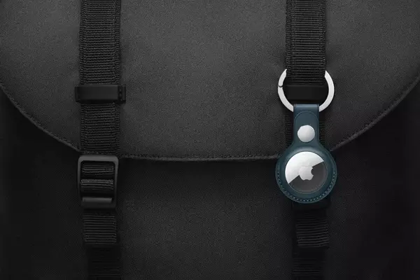 A close up of an AirTag keychain on a black backpack