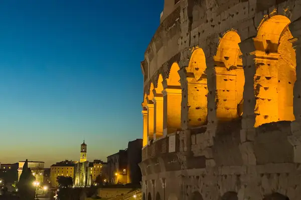 The Colosseum at night in Rome, illuminated with city buildings in the background