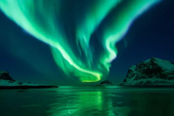 Northern lights over a snowy landscape with mountains and a reflective body of water