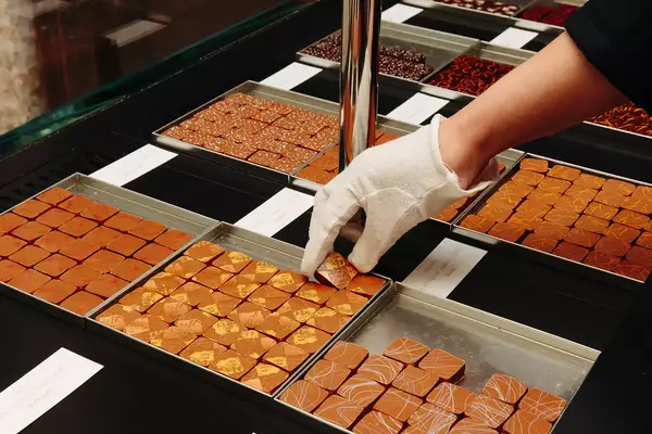 A hand wearing a white glove prepares chocolates in France