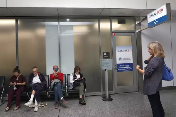 A line of people (left) wait for their Global Entry interview appointments at San Francisco International airport as Gayle Collins (right) tries to find out the status of her application 