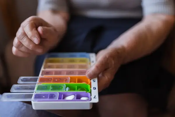 A person handling a weekly pill organizer box containing different medications