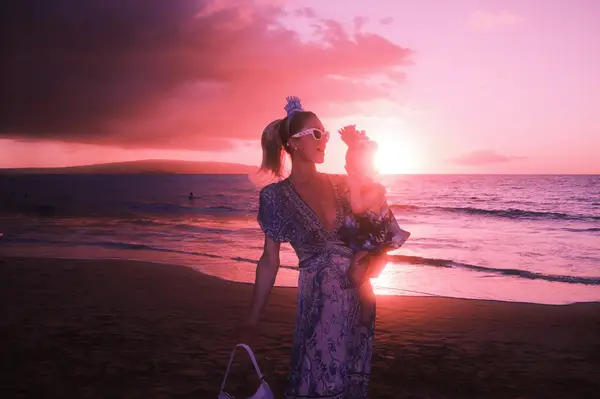 A woman holding a child stands on a beach at sunset