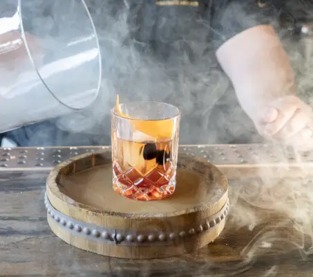 bartender serves a smoked old fashion cocktail