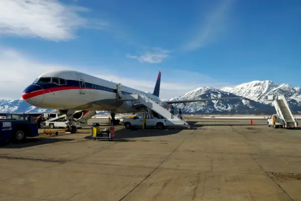 people boarding a jet airplane with snow covered mountains in background