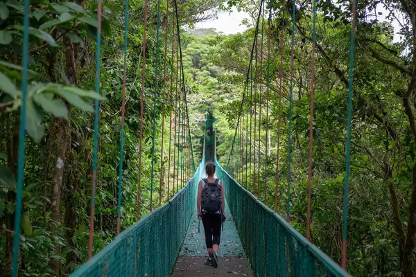 Woman walking across hanging bridge with backpack on in Monteverde, Costa Rica