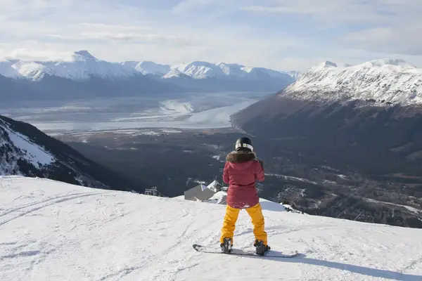 Woman stands on snowboard at the top of the mountain in Girdwood, Alaska