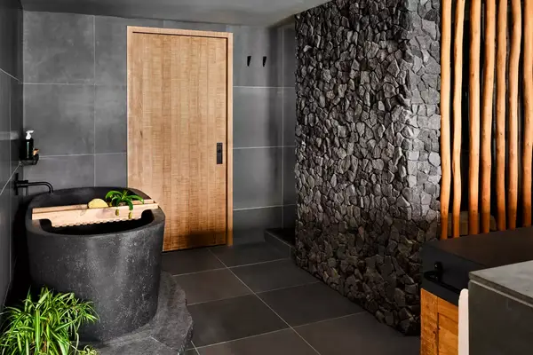 Suite guest bath with black standing tub and rock wall 