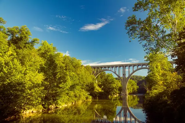 Bridge spanning a river surrounded by trees, clear sky and water reflections.
