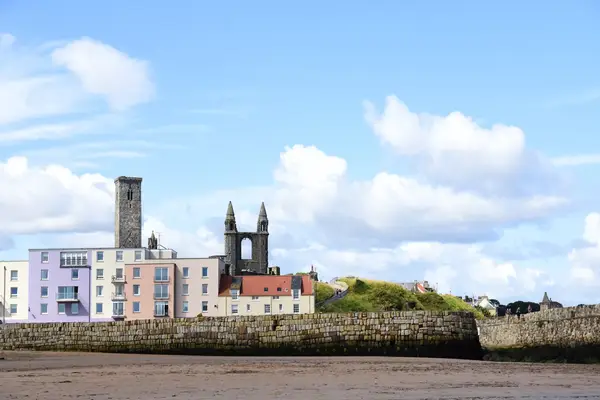 View of a waterfront area with buildings and a stone wall, including notable church ruins in the background