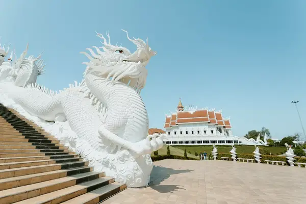 A large white dragon sculpture near a temple with red roof in Chiang Rai