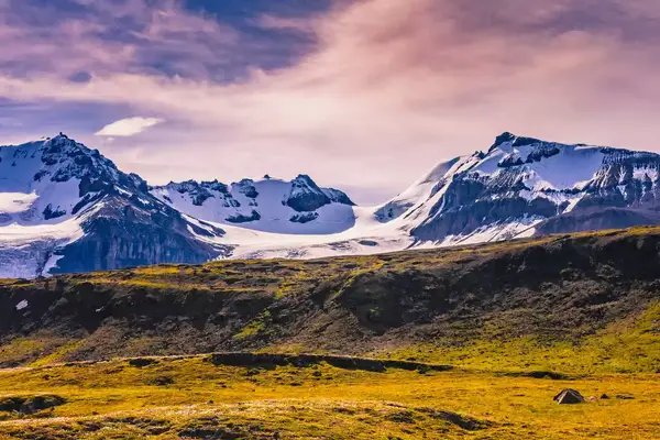 Snow-capped mountains under a cloudy sky with grasslands in the foreground