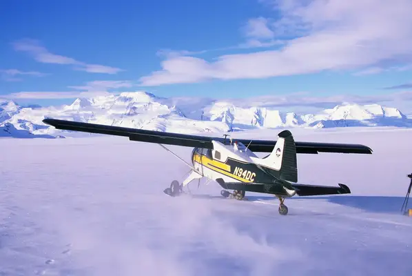 A small airplane parked on a snowy field with mountains in the background