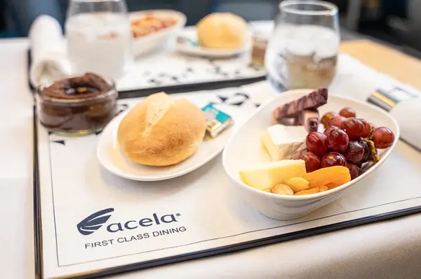 A tray with food items served in Acela First Class Dining including a bread roll fruit and various accompaniments