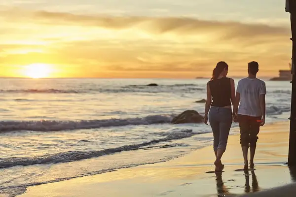 A couple walks along a beach at sunset