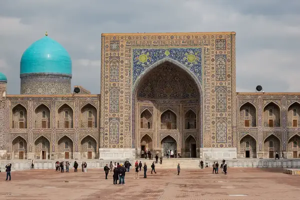The Registan Square in Samarkand, showcasing intricate Islamic architecture and blue domes with scattered visitors