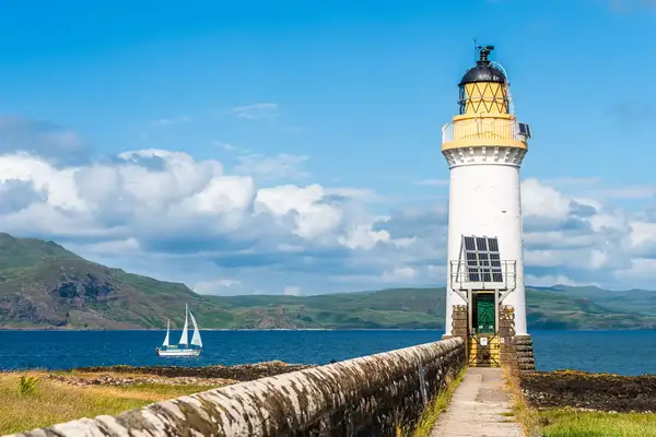 A lighthouse near a body of water with a sailboat in the background