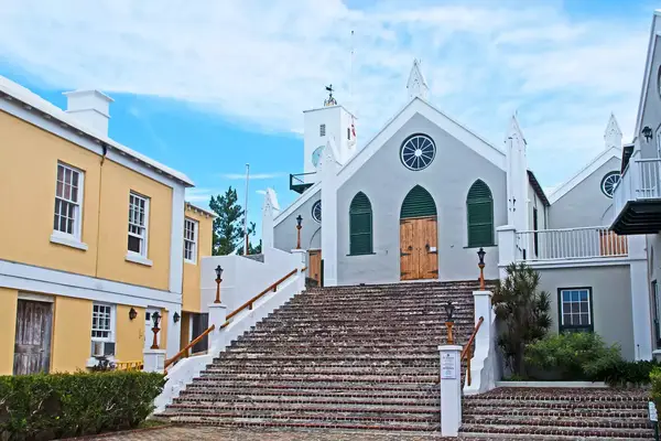 A colonial-style church and surrounding buildings in a town square setting, featuring prominent stairs and Bermuda architecture