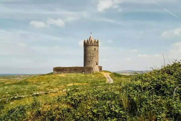 A stone tower stands on a grassy hill with a pathway leading to it