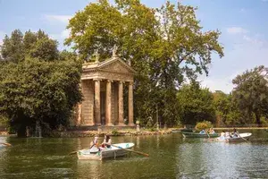 Small boats in a lake near a classical temple surrounded by trees, a scene in Villa Borghese Gardens, Rome