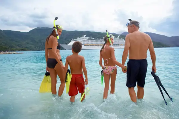 A family with snorkel gear walking towards a cruise ship in the ocean