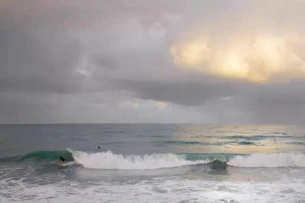 Panoramic scene of a surfer riding a wave after a rain squall has passed at the Sebastian Inlet State Park in Florida.