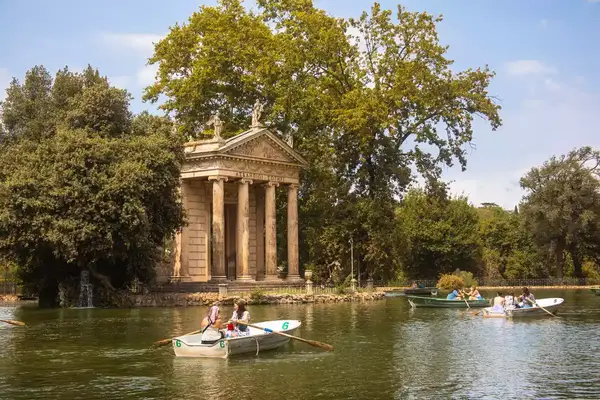 Small boats in a lake near a classical temple surrounded by trees, a scene in Villa Borghese Gardens, Rome
