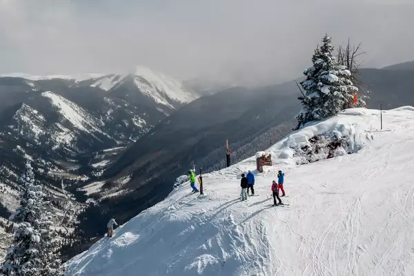 A group of skiers and snowboarders wait to head down a steep trail at Aspen Highlands ski area in Aspen, Colorado, USA.