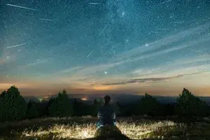 A person sitting outdoors under the night sky during a meteor shower