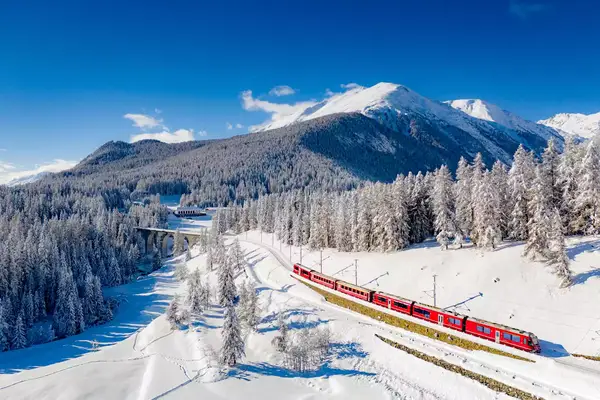 Bernina Express train traveling in the alpine valley covered with snow, Chapella, Graubunden canton, Engadine, Switzerland