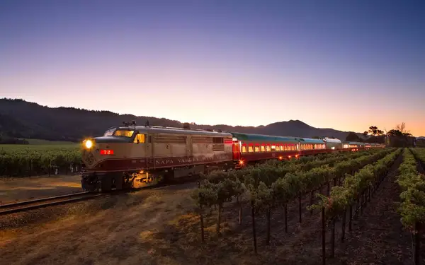 Napa Valley Wine Train cruising between vineyards at sunset.