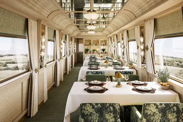 Elegant dining area inside a train car with neatly set tables and a view of the landscape through the windows, featuring vintage decor