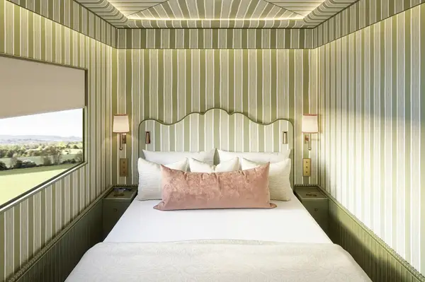 Nicely decorated bedroom with a striped wall pattern and a scenic window view, featuring a bed with accent pillows and lit lamps