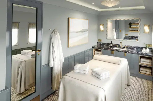 Interior of a spa room with treatment table, mirror, robes, towels, and wall-mounted fixtures