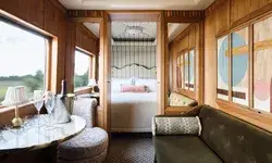 Elegant train cabin with a seating area table with champagne and a bed in the background
