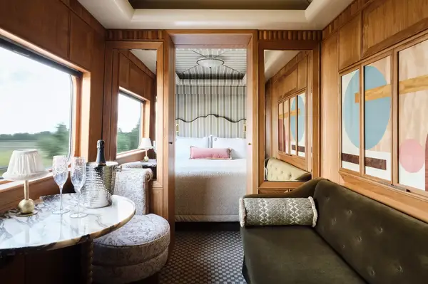 Elegant train cabin with a seating area table with champagne and a bed in the background