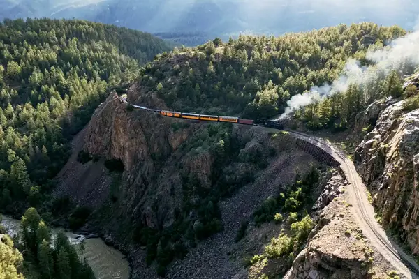 Drone view of the Durango & Silverton train with cliffs and forest on either side of the track