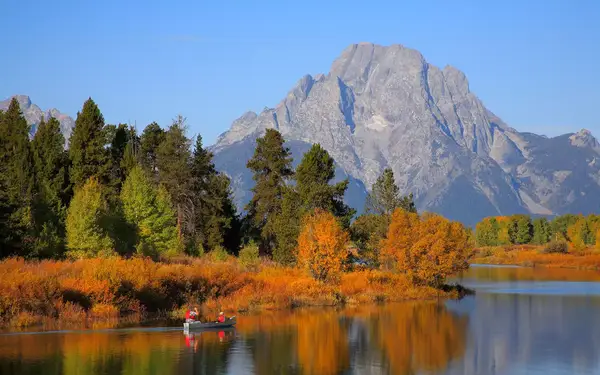 Lake surrounded by orange-colored trees and a large peak