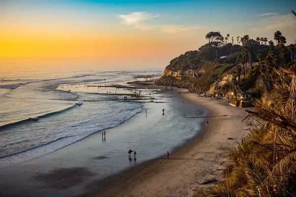 A scenic view of a beach and cliffs during sunset with people walking along the shore