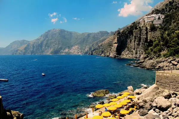 A coastal scene with rocky cliffs and the sea, yellow umbrellas on a lower viewing point