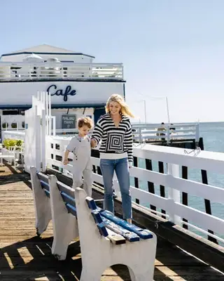 Amanda Kloots and Elvis hold hands as he walks along a bench at the pier 