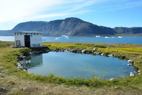 Pool of hot water near a lake and mountains on a sunny day in Uunartoq, Greenland