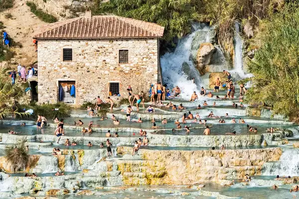 Several people gather and spread out at Cascate del Mulino waterfall and hot springs, Saturnia thermae in Tuscany.