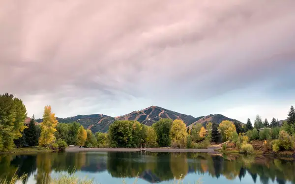 The mountains of Sun Valley, Idaho, peek over the edge of a serene, tree-shaded lake.