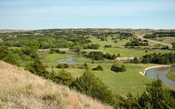 A winding stream cuts through the grassy, tree-covered hills of Nebraska